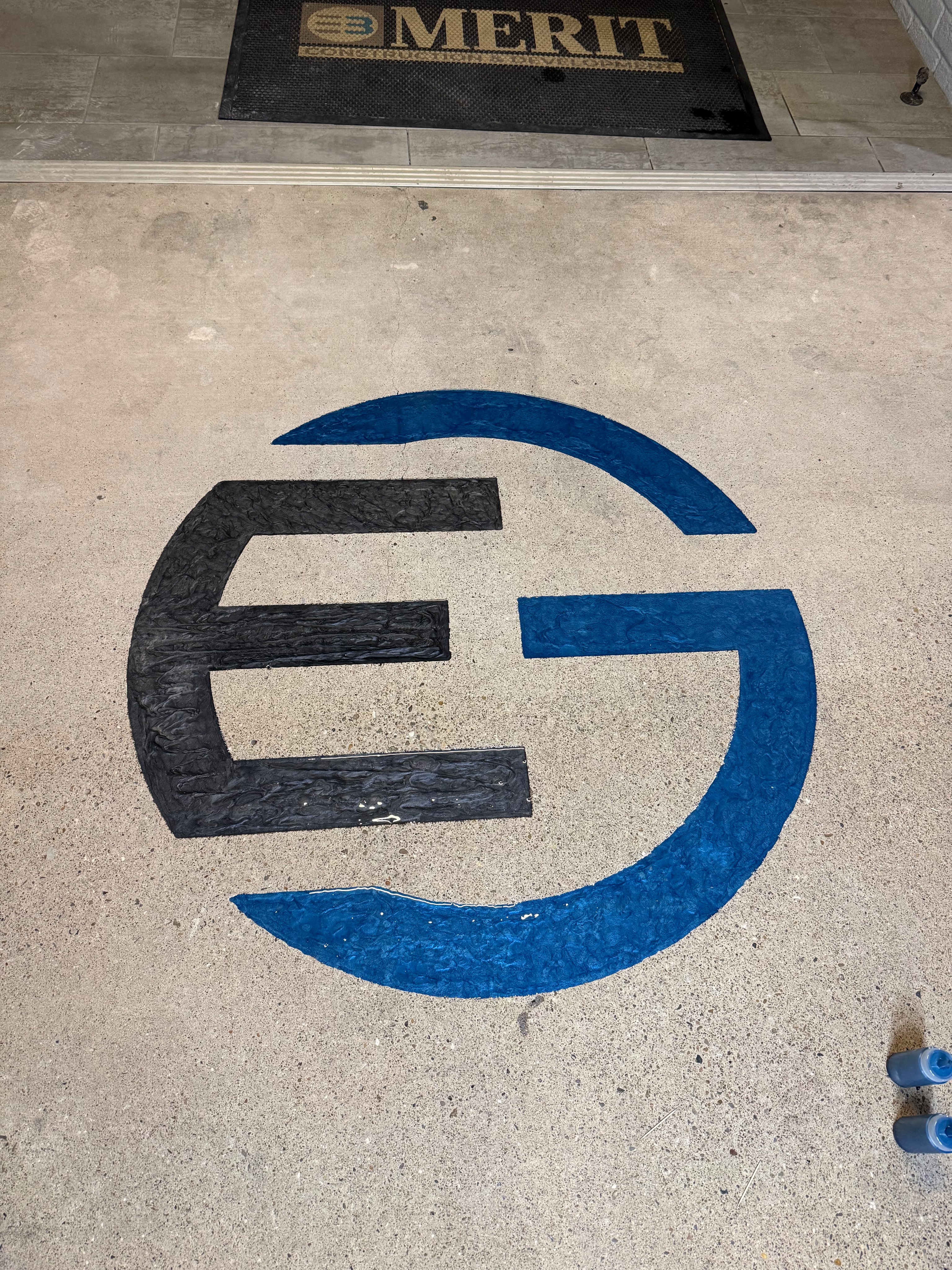 Merit Construction EG logo engraved in black and blue